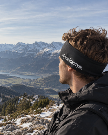 Wanderer steht in den Bergen und trägt schwarzes Stirnband.